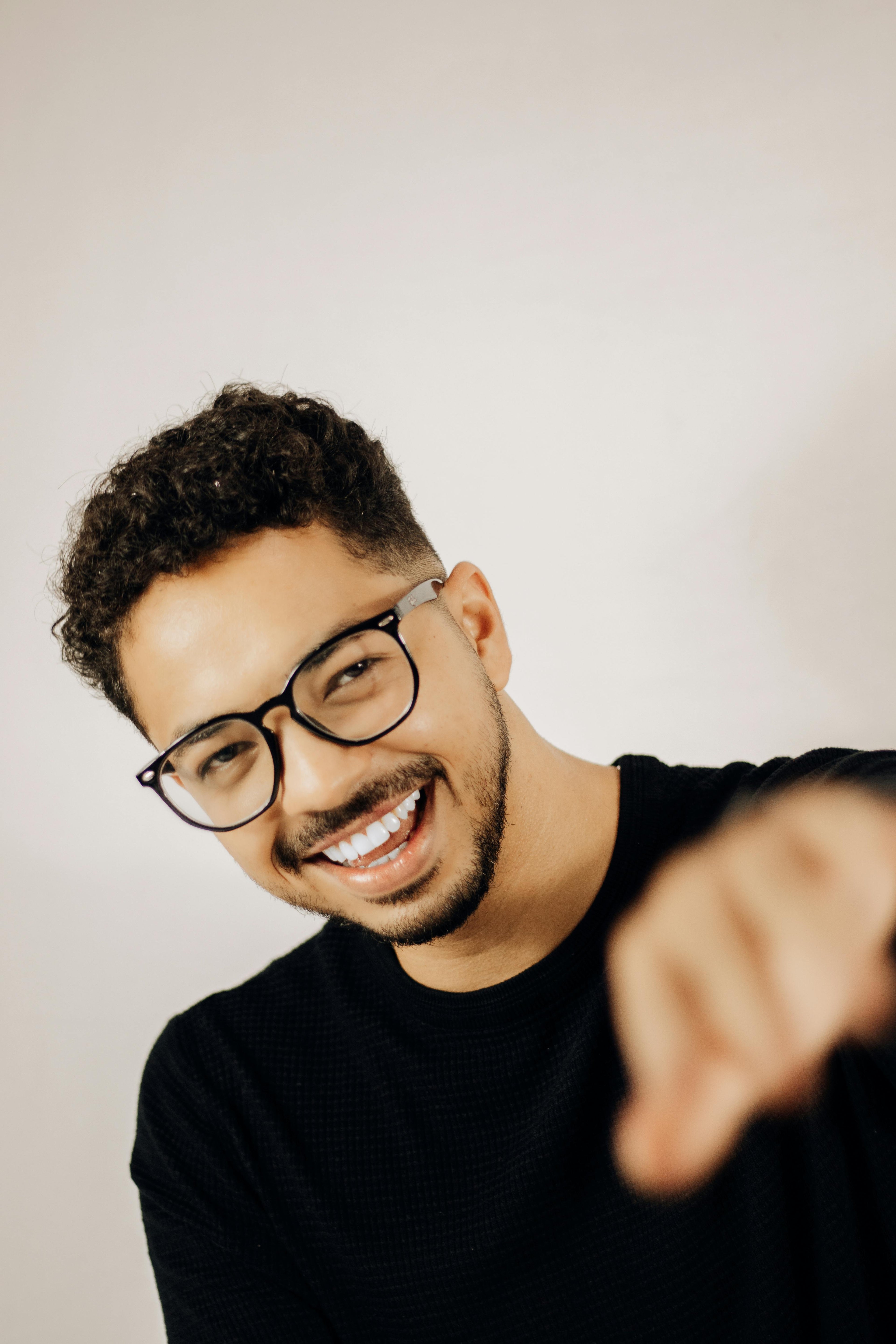 a smiling man styling a stylish frame in black shirt on a egg white background