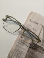 Olive green rectangular eyeglasses resting on a newspaper, modern optical frames for daily wear