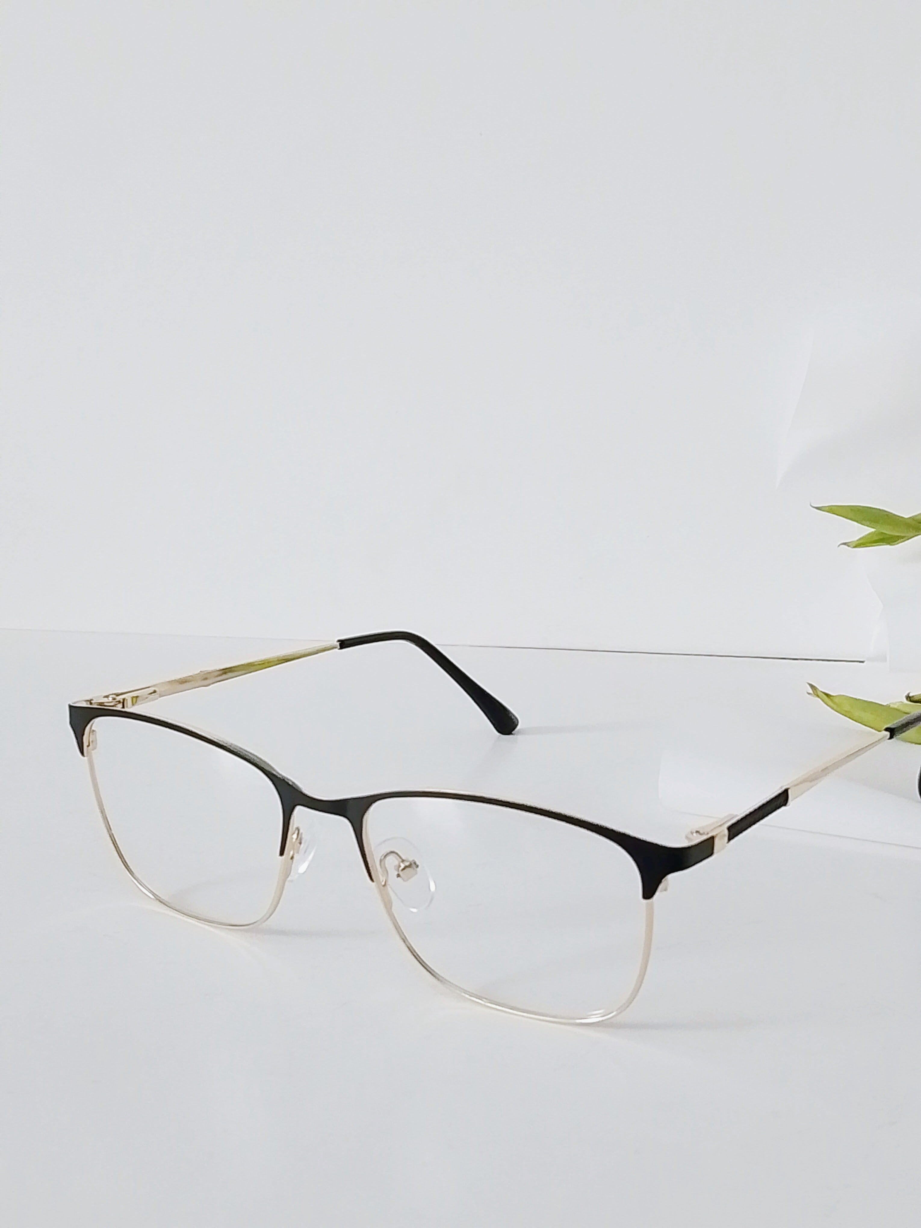 Stylish black and gold half-rim eyeglasses with clear lenses on white surface, modern optical frames
