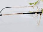 Gold-rimmed glasses with black textured temples, clear lenses, on white surface with green leaf blur
