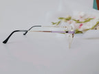 Elegant rimless glasses with lavender temple accents, sleek black arms, and gold detailing on white surface with floral backdrop