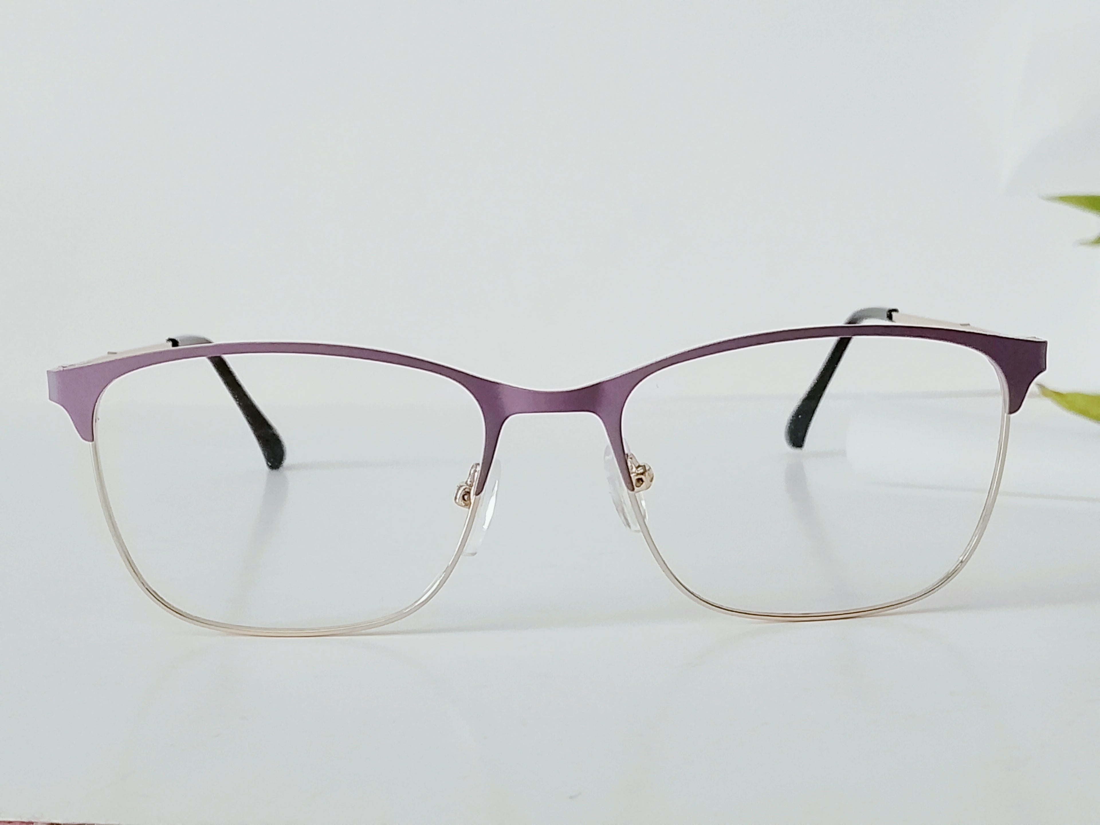 Purple and silver metal eyeglass frames with clear lenses on white surface