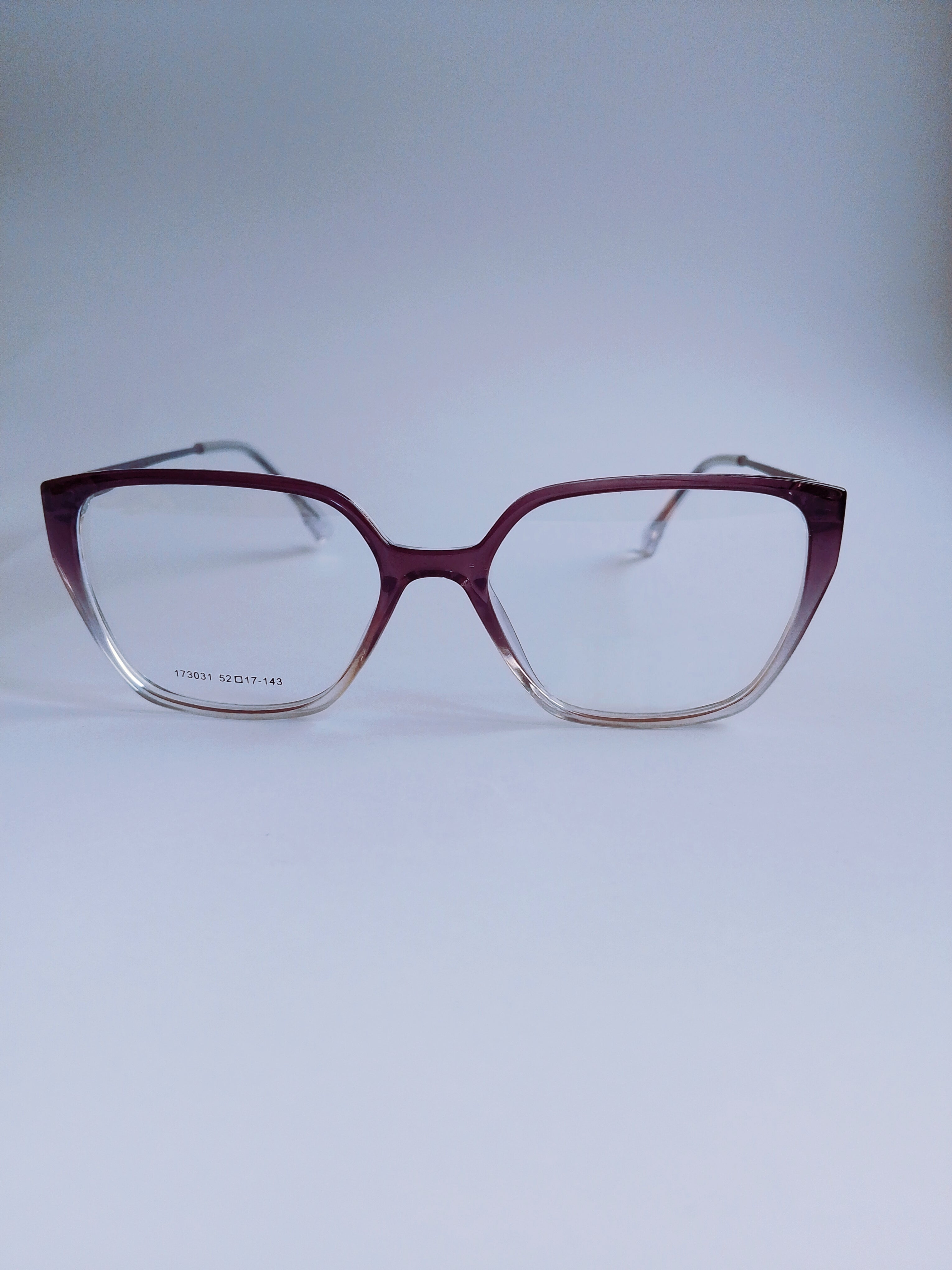 A pair of cat- eye eyeglasses with a translucent burgundy acetate frame that fades to clear at the bottom, shown against a light gray background.