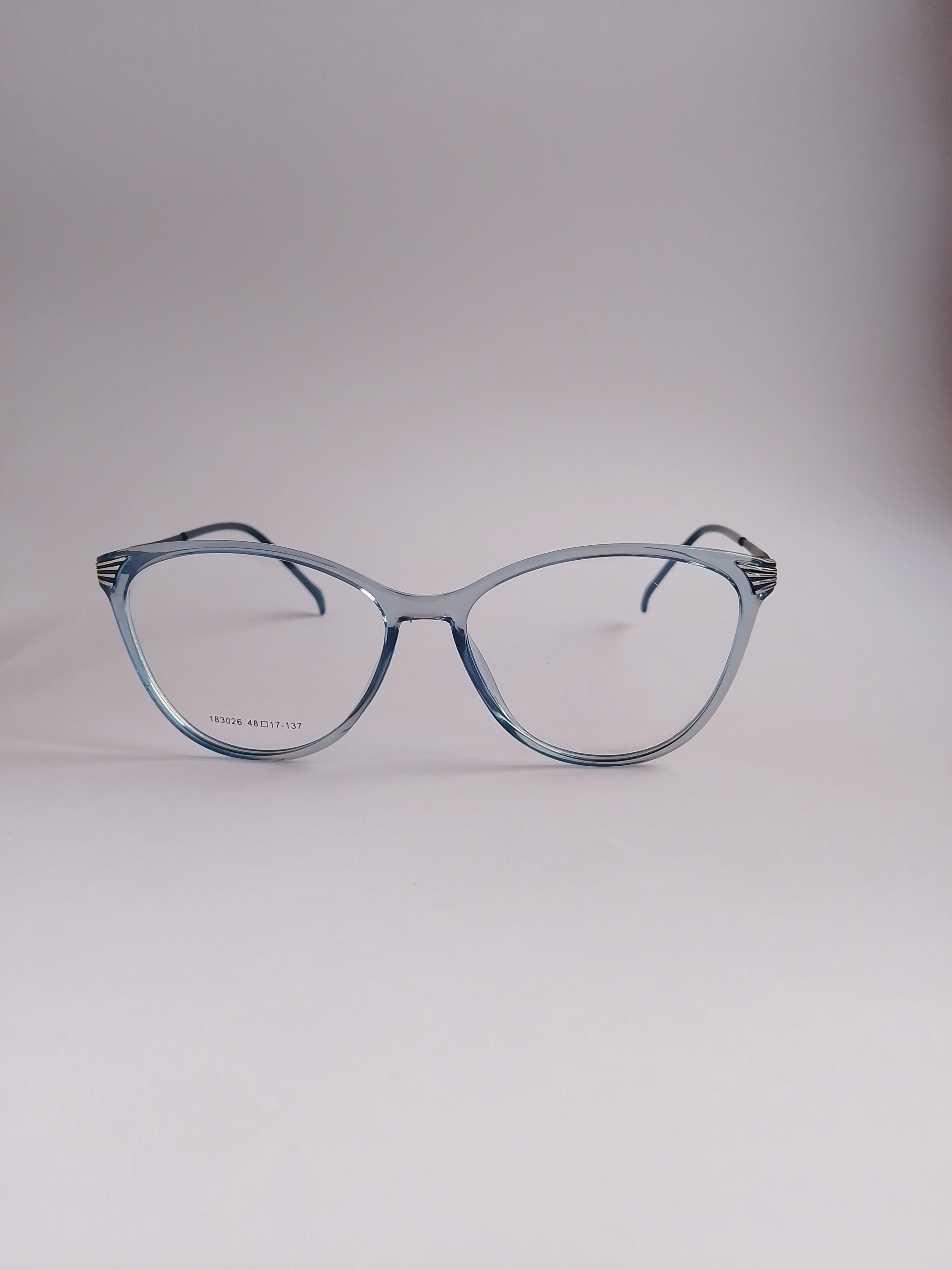 A pair of classic cat-eye eyeglasses with a translucent light blue acetate frame, displayed on a neutral light gray background.