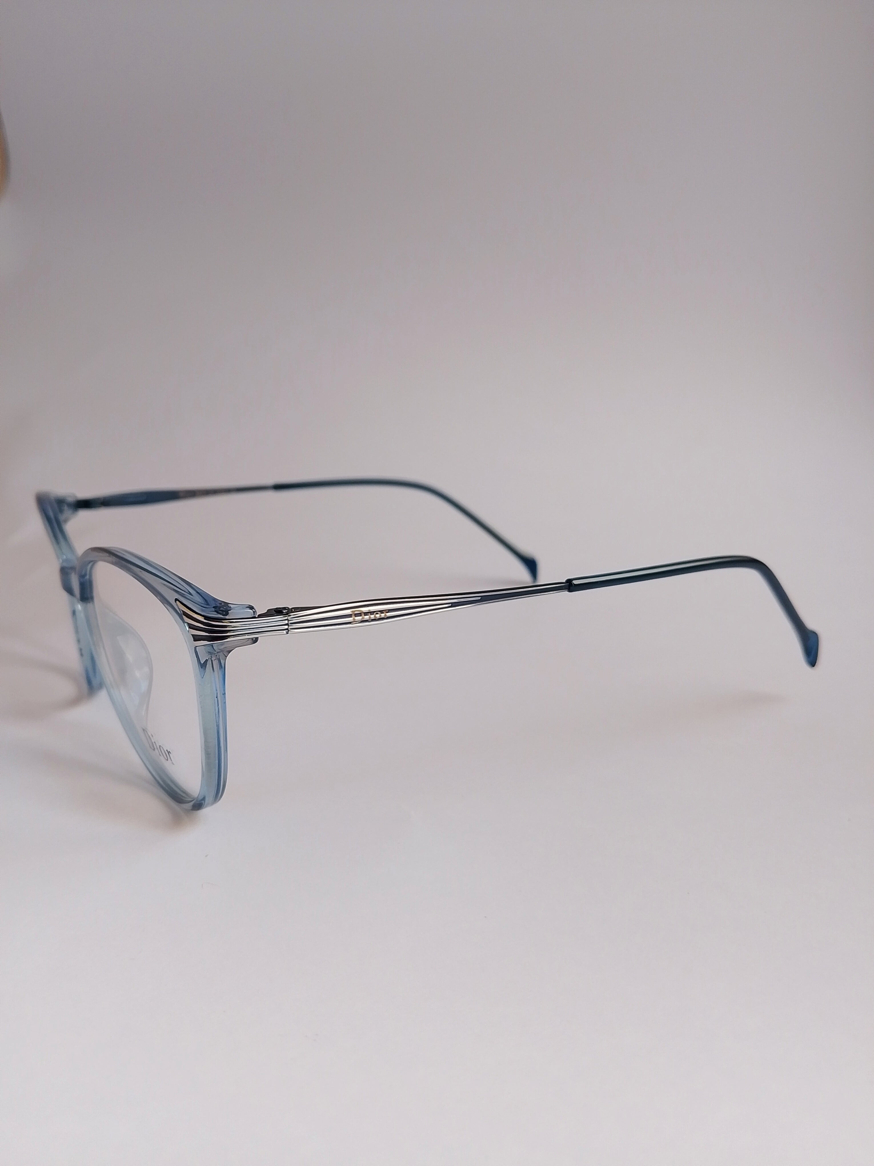 Light blue acetate eyeglass frames with a silver metal double bridge and thin dark blue temples, shown on a neutral light gray background.