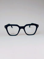 A pair of thick, dark navy blue acetate eyeglass frames with a unique geometric, slightly angular square shape. The clear lenses are visible, and the inner temple arms are a contrasting teal green.