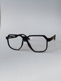 A pair of oversized square eyeglasses with a matte black frame and dark brown patterned temples, shown on a plain light gray background.