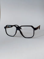 A pair of oversized square eyeglasses with a matte black frame and dark brown patterned temples, shown on a plain light gray background.
