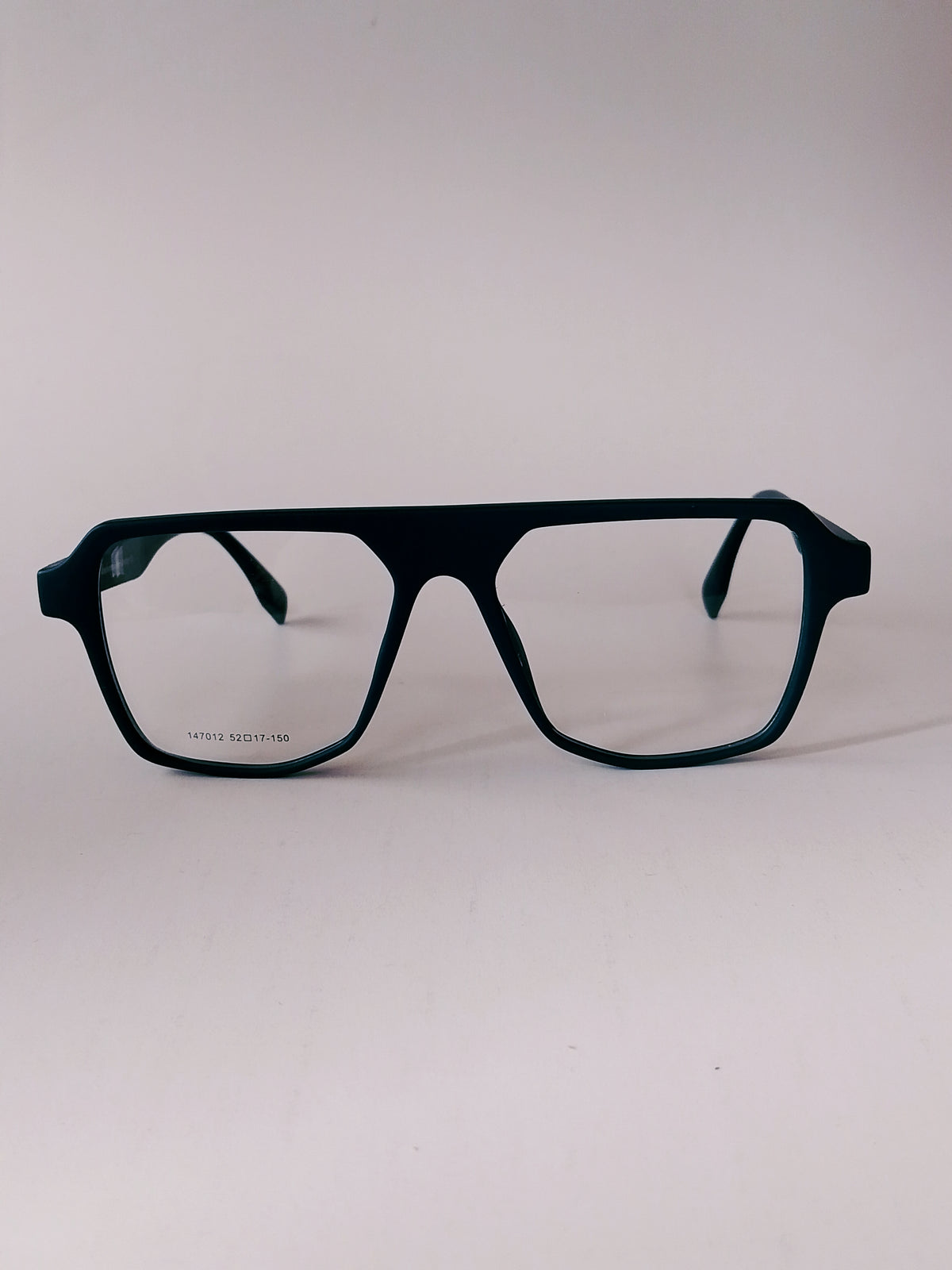 A pair of oversized square eyeglasses with a matte black frame and clear lenses, photographed against a neutral light gray background.