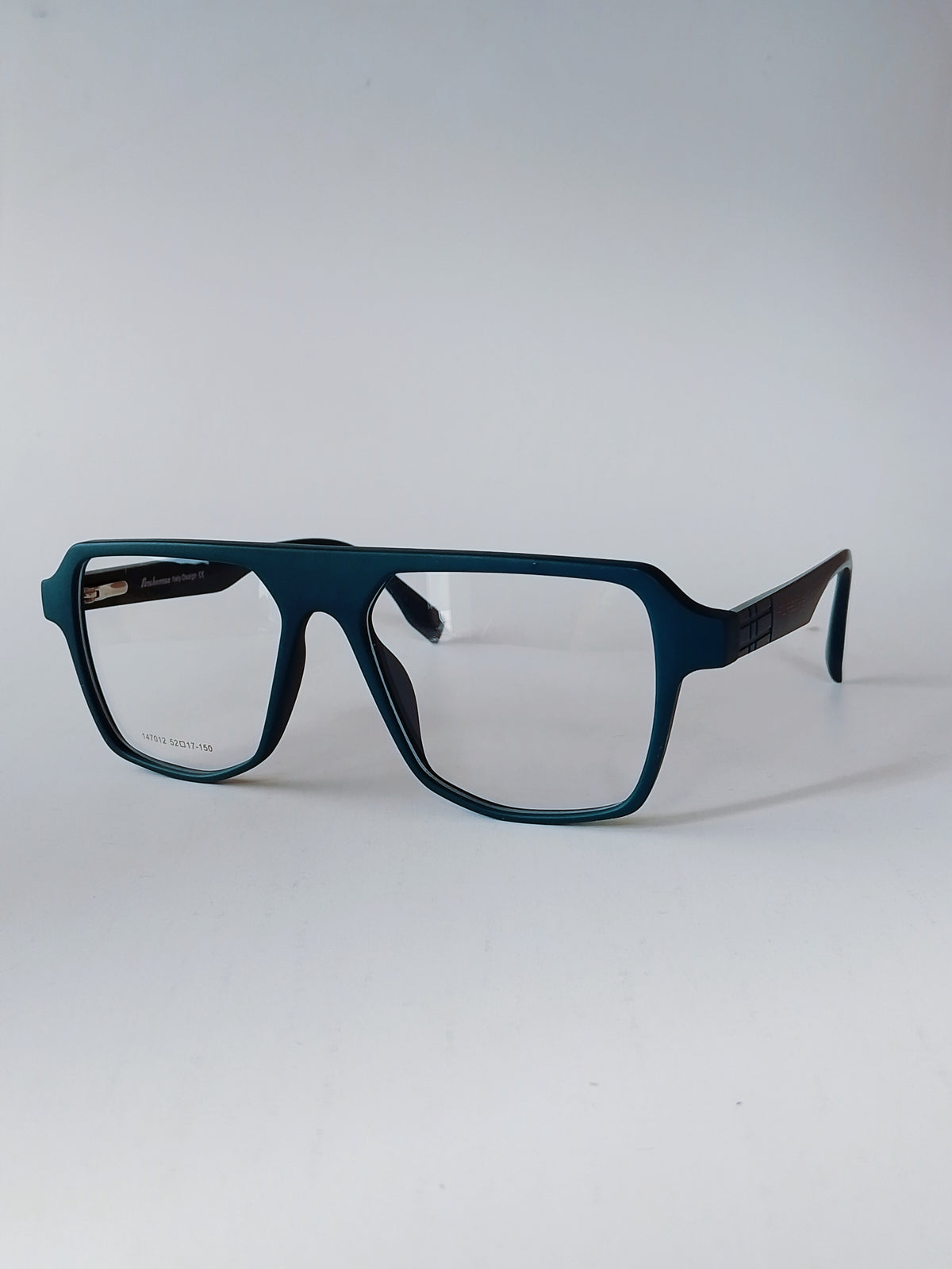 Matte dark teal blue eyeglasses with a thick square frame and clear lenses, shown from a three-quarters angle on a light gray background.