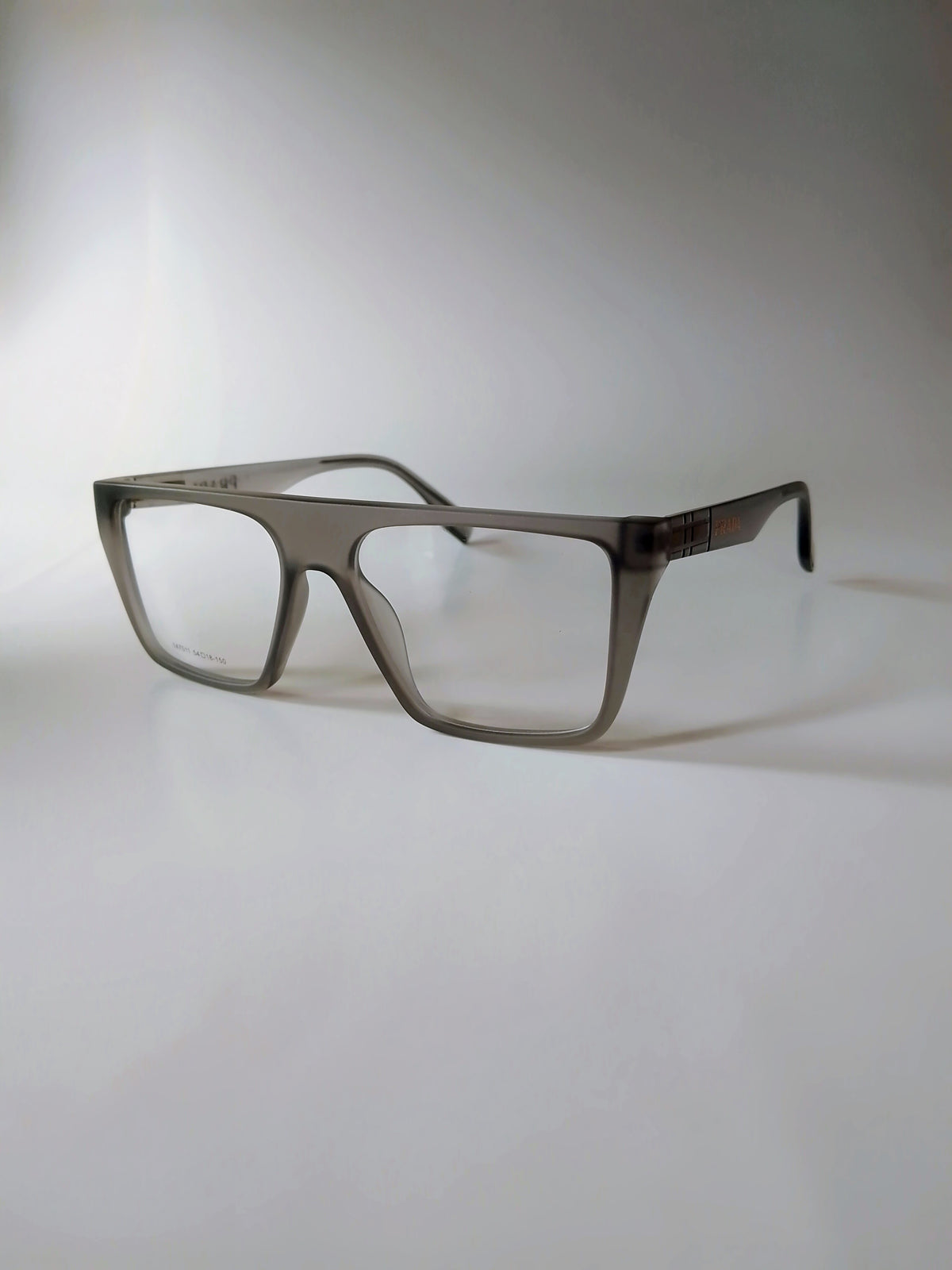 A pair of square-frame eyeglasses with a translucent taupe-gray acetate frame and clear lenses, resting on a light gray surface against a neutral background.