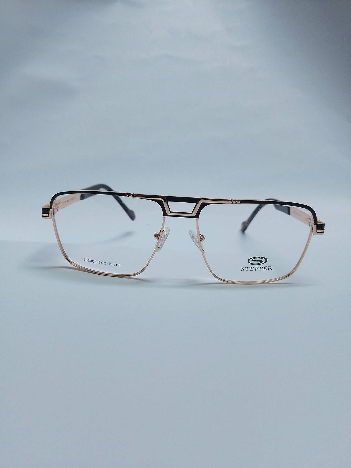 A pair of Stepper brand aviator-style eyeglasses with a rose gold metal frame, featuring a black double bridge and black temple tips, resting on a light gray surface.