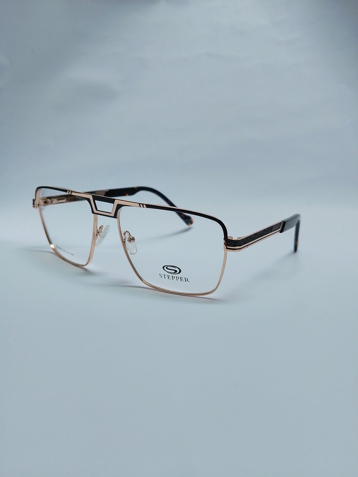 A pair of semi-rimless eyeglasses with a metallic rose gold frame and dark temples, displayed on a light gray background. 
