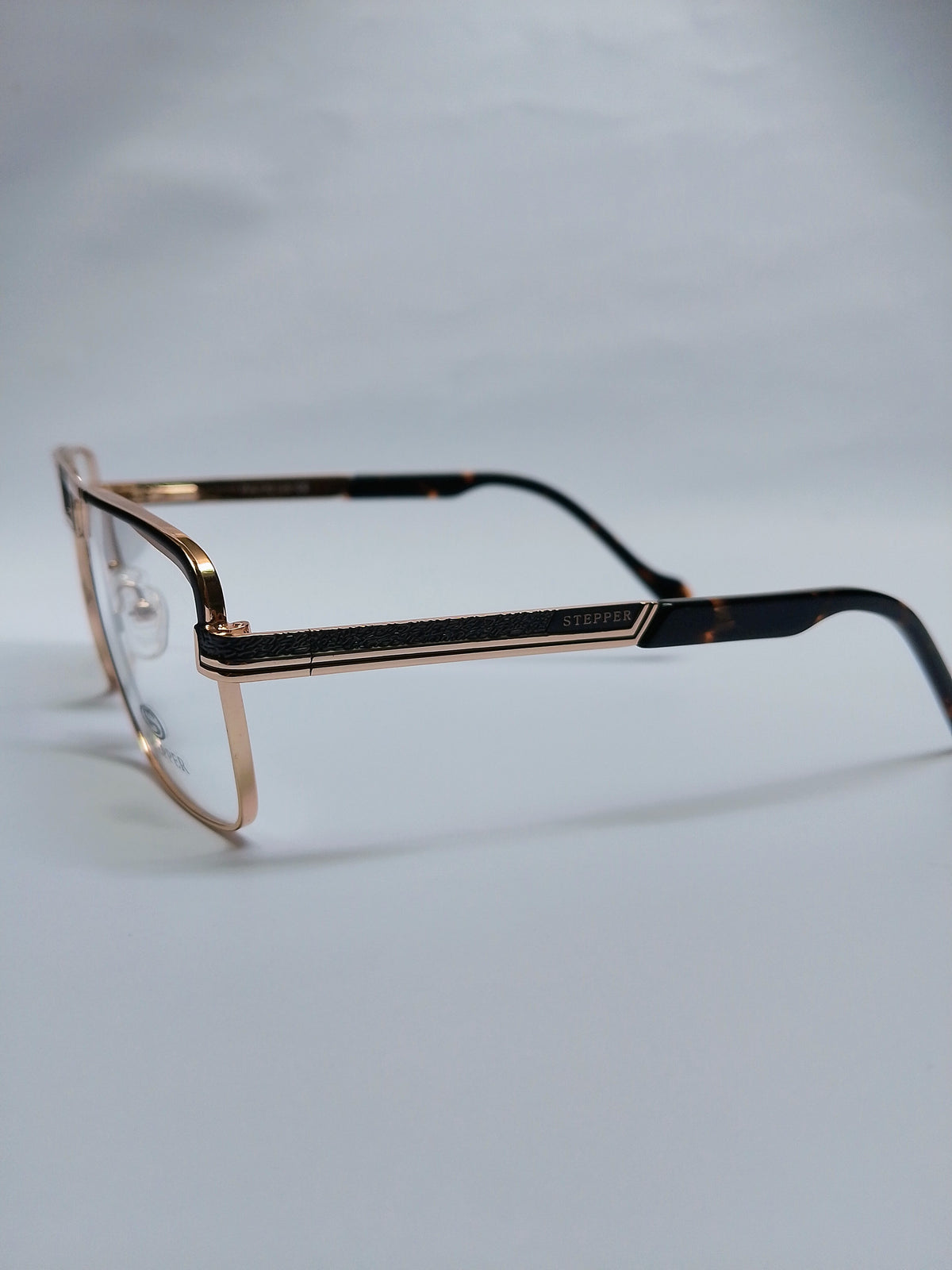 A pair of eyeglasses with a gold-tone metal frame and dark tortoiseshell temples, displayed on a light gray background.