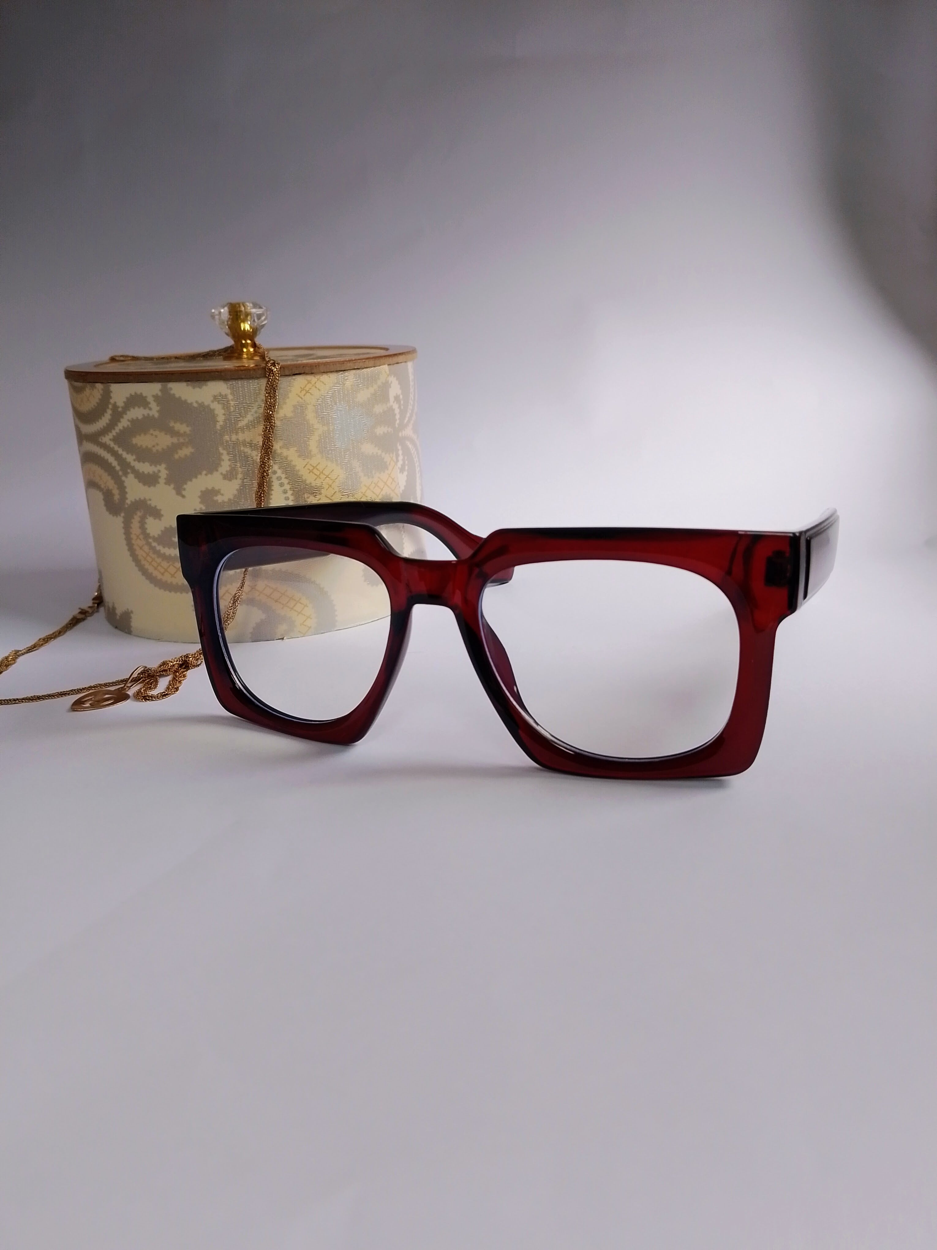 a meroon shade oversize frame with white backgroud aong with jwellery box and gold jewllery 