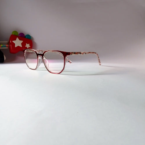 A pair of round eyeglasses with a translucent pink and red acetate frame and patterned temples, resting on a white surface against a light background.