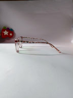 A pair of clear-framed eyeglasses with thin, patterned arms featuring red, green, and black details, resting on a white surface against a white background.