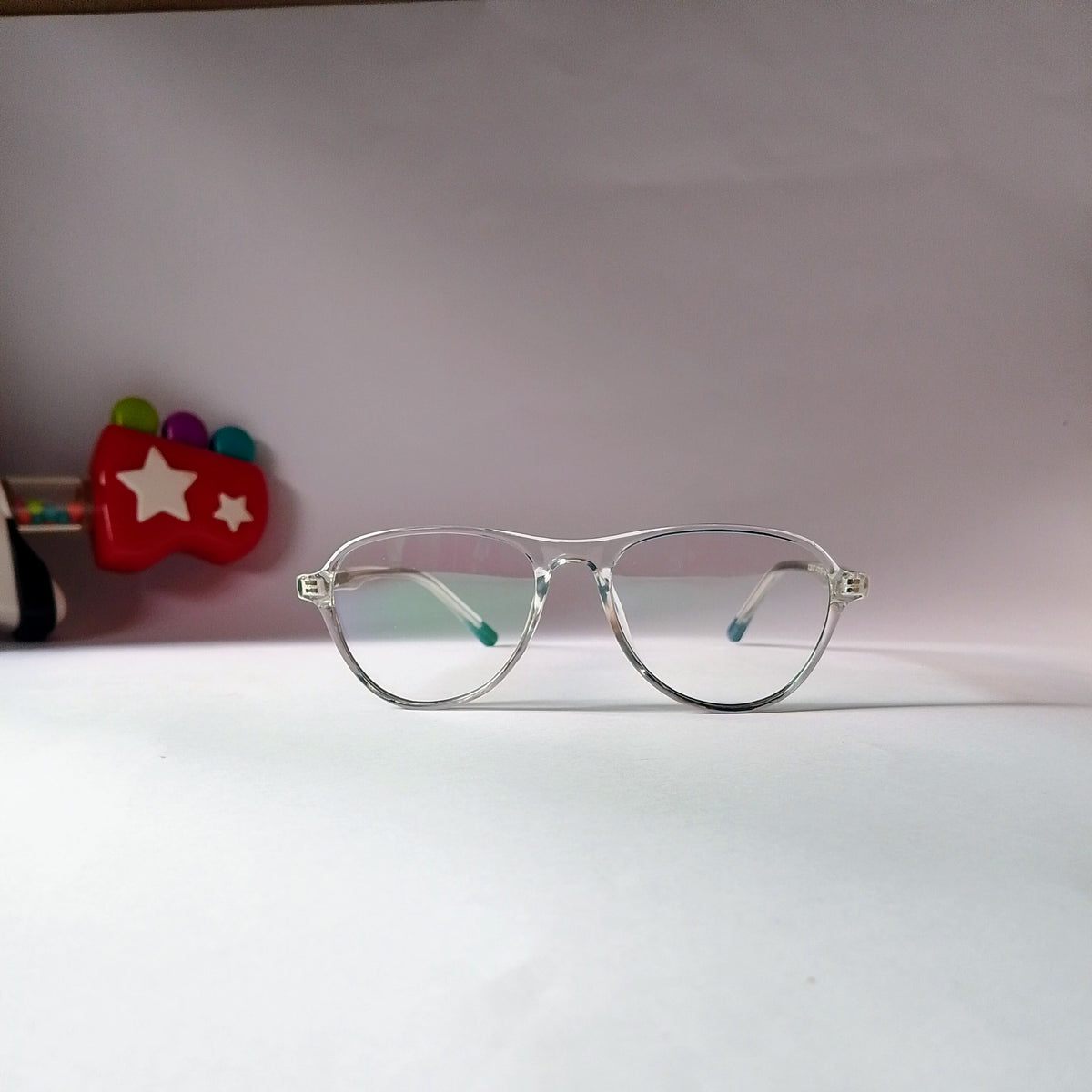 A pair of clear-framed eyeglasses with light blue-tinted lenses, resting on a white surface against a light pink background.