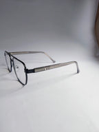 A pair of square aviator-style eyeglasses with a black front frame and silver metal temples, resting on a white surface against a gray background.