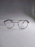 A pair of aviator-style eyeglasses with a thin rose gold metal frame and clear lenses, resting on a neutral gray surface.