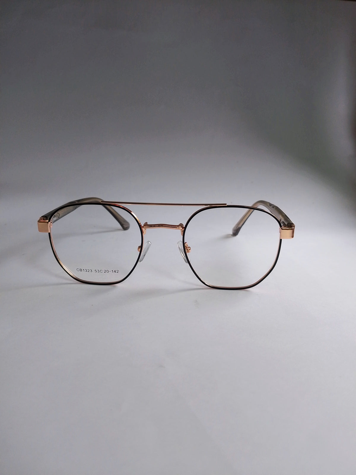 A pair of aviator-style eyeglasses with a thin rose gold metal frame and clear lenses, resting on a neutral gray surface.