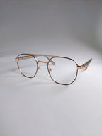 A pair of aviator-style eyeglasses with a thin rose gold metal frame and clear lenses, resting on a light gray surface against a neutral gray background.