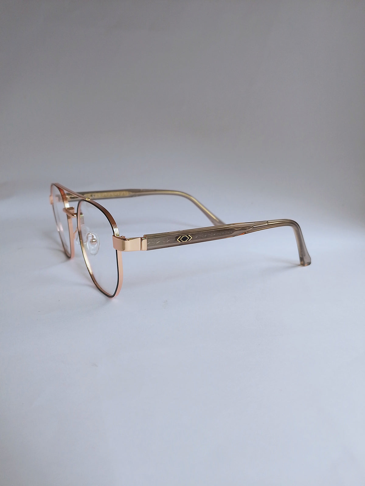 Vintage metal eyeglasses with a rose gold-toned frame and clear lenses, displayed on a neutral light gray background.
