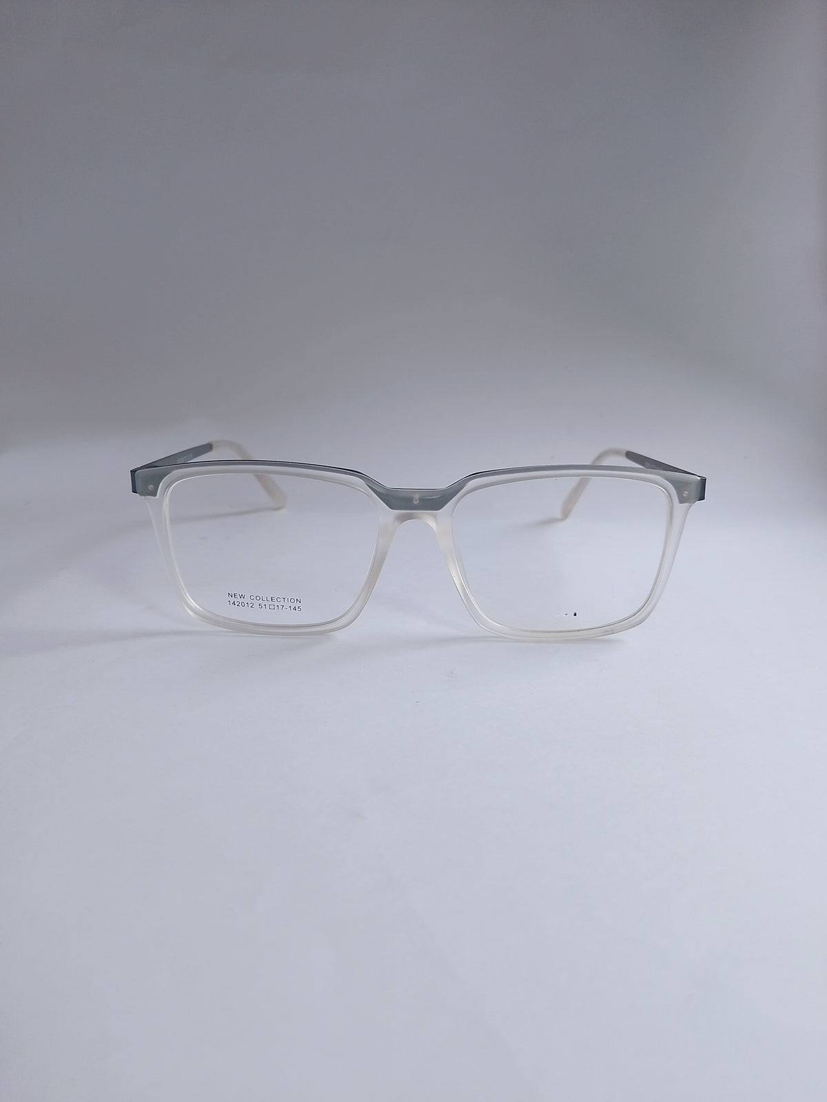 A pair of square-framed eyeglasses with a translucent clear acetate body and a contrasting silver metal top bar, shown on a neutral light gray background.