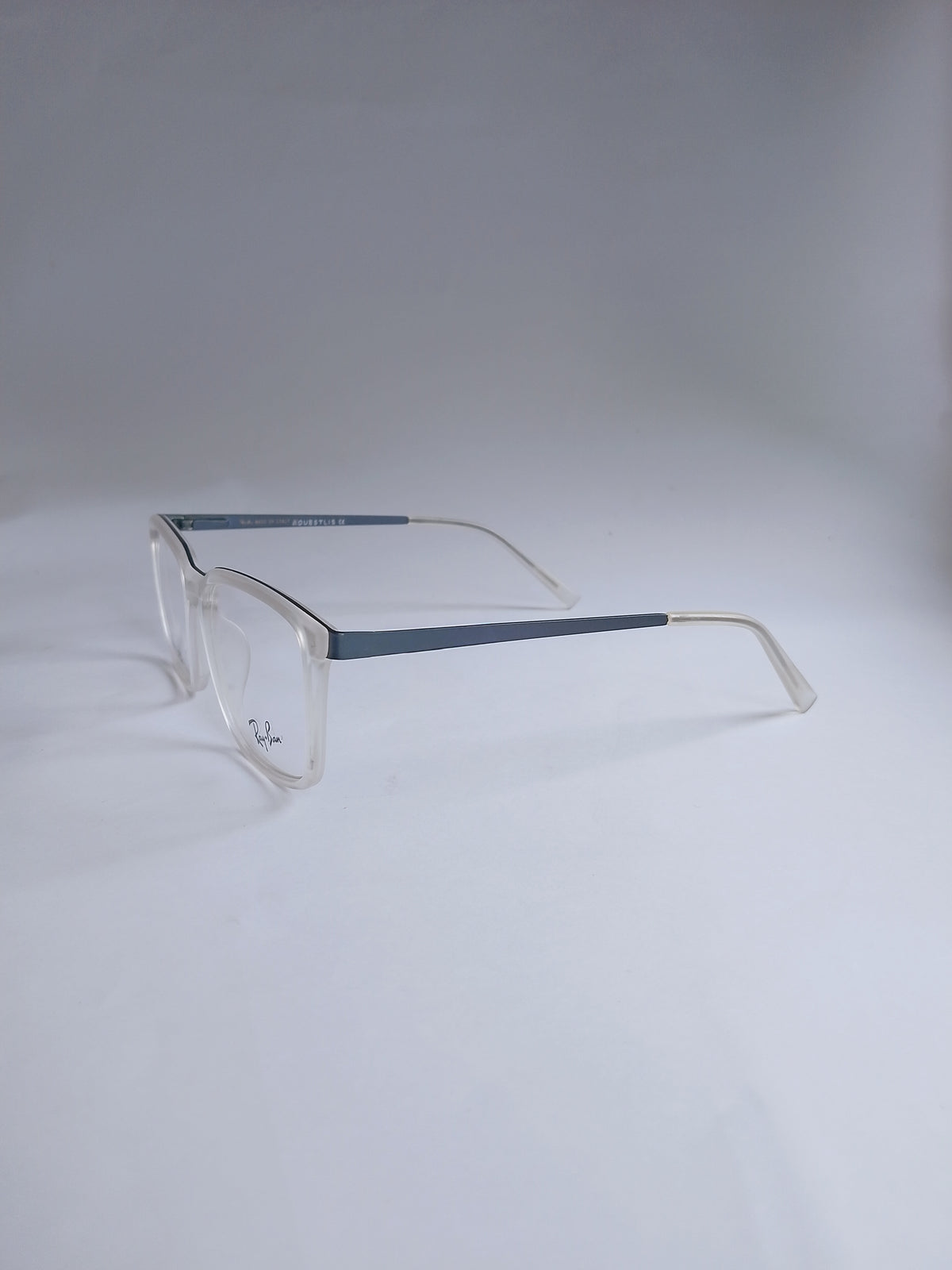 A pair of square-frame eyeglasses with clear acetate frames and slim blue temples, photographed on a light gray studio background.