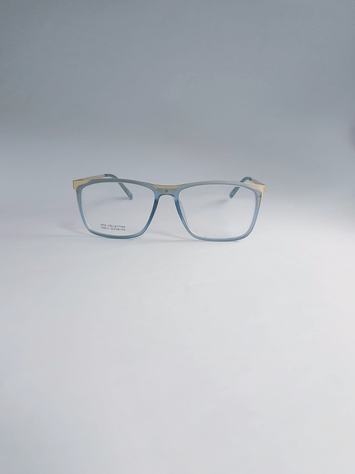 A pair of square eyeglasses with a translucent light blue acetate frame and gold metal temples, displayed on a clean light gray background.