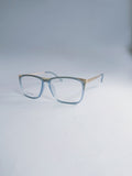 A pair of square eyeglasses with a translucent light blue acetate frame and a thin gold metal bridge and temples, displayed on a light gray studio background.