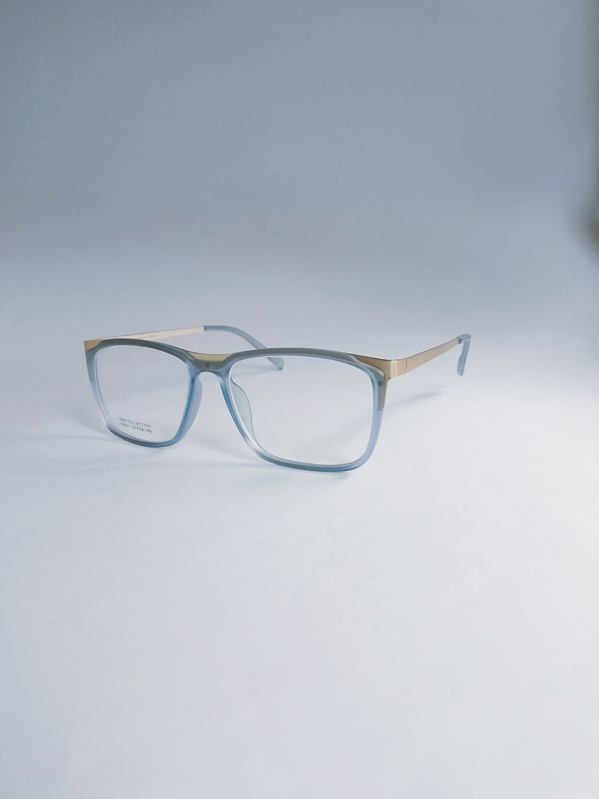 A pair of square eyeglasses with a translucent light blue acetate frame and a thin gold metal bridge and temples, displayed on a light gray studio background.