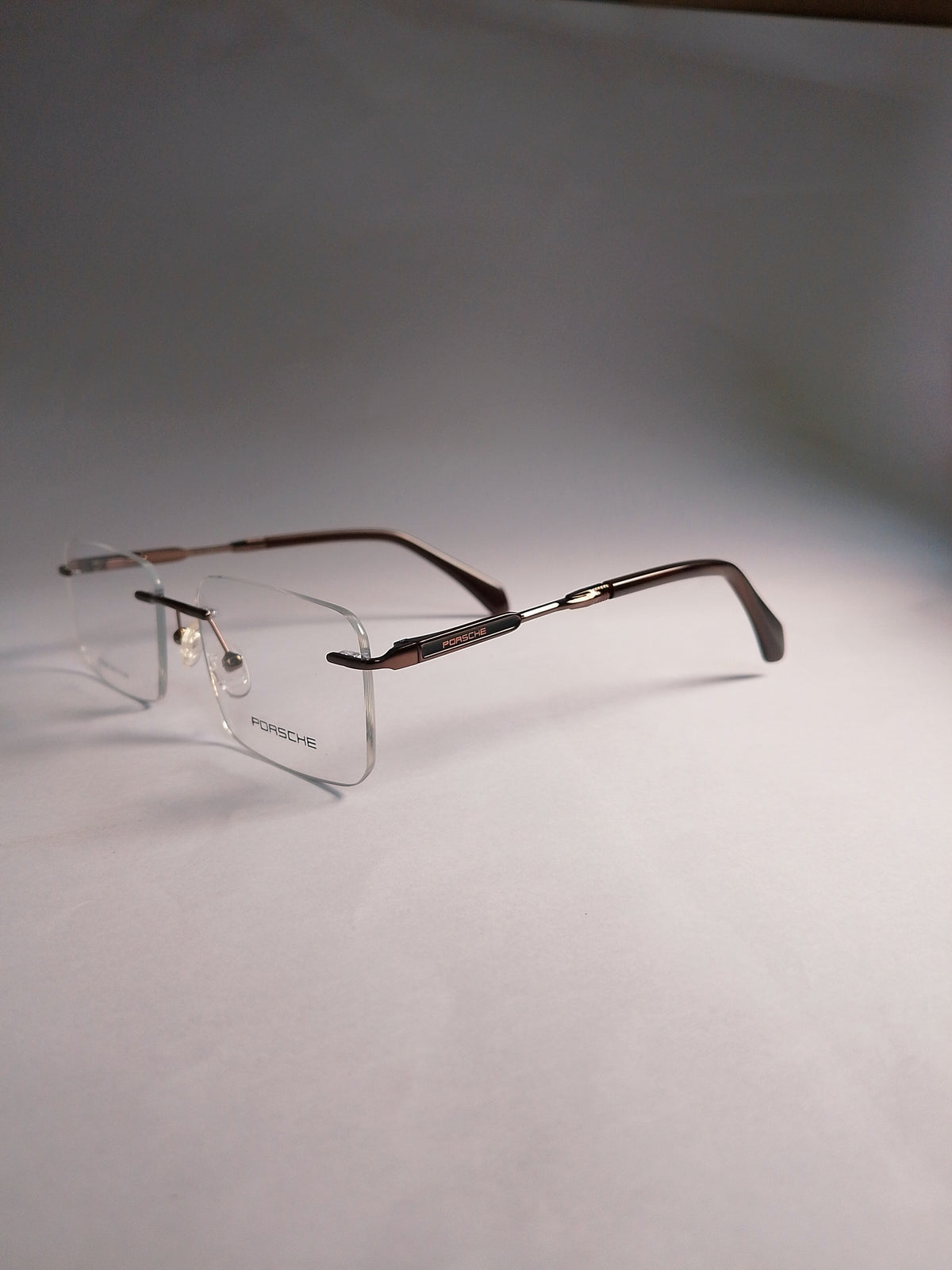  rimless eyeglasses with a dark brown woodgrain finish on the temples and clear lenses, displayed on a neutral gray background.