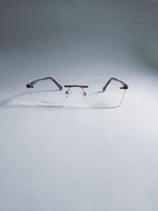 A pair of rimless eyeglasses with clear lenses and dark brown temples, displayed on a light gray gradient studio background.