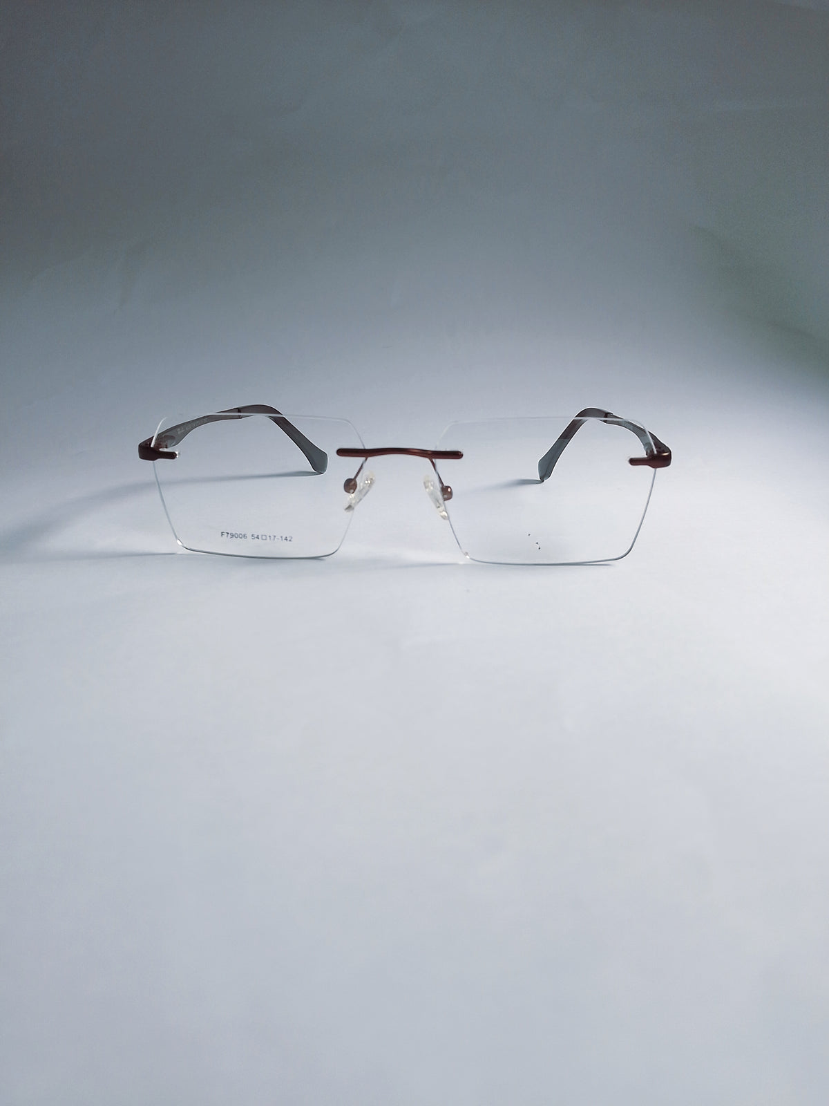 A pair of rimless eyeglasses with clear lenses and dark brown temples, displayed on a light gray gradient studio background.