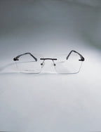 A pair of rimless eyeglasses with a thin black metal frame and clear lenses, displayed on a light gray background.