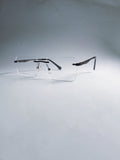 A pair of rimless square eyeglasses with clear lenses and dark metal temples, displayed on a light gray gradient background.