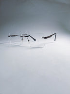 A pair of rimless square eyeglasses with clear lenses and dark metal temples, displayed on a light gray gradient background.
