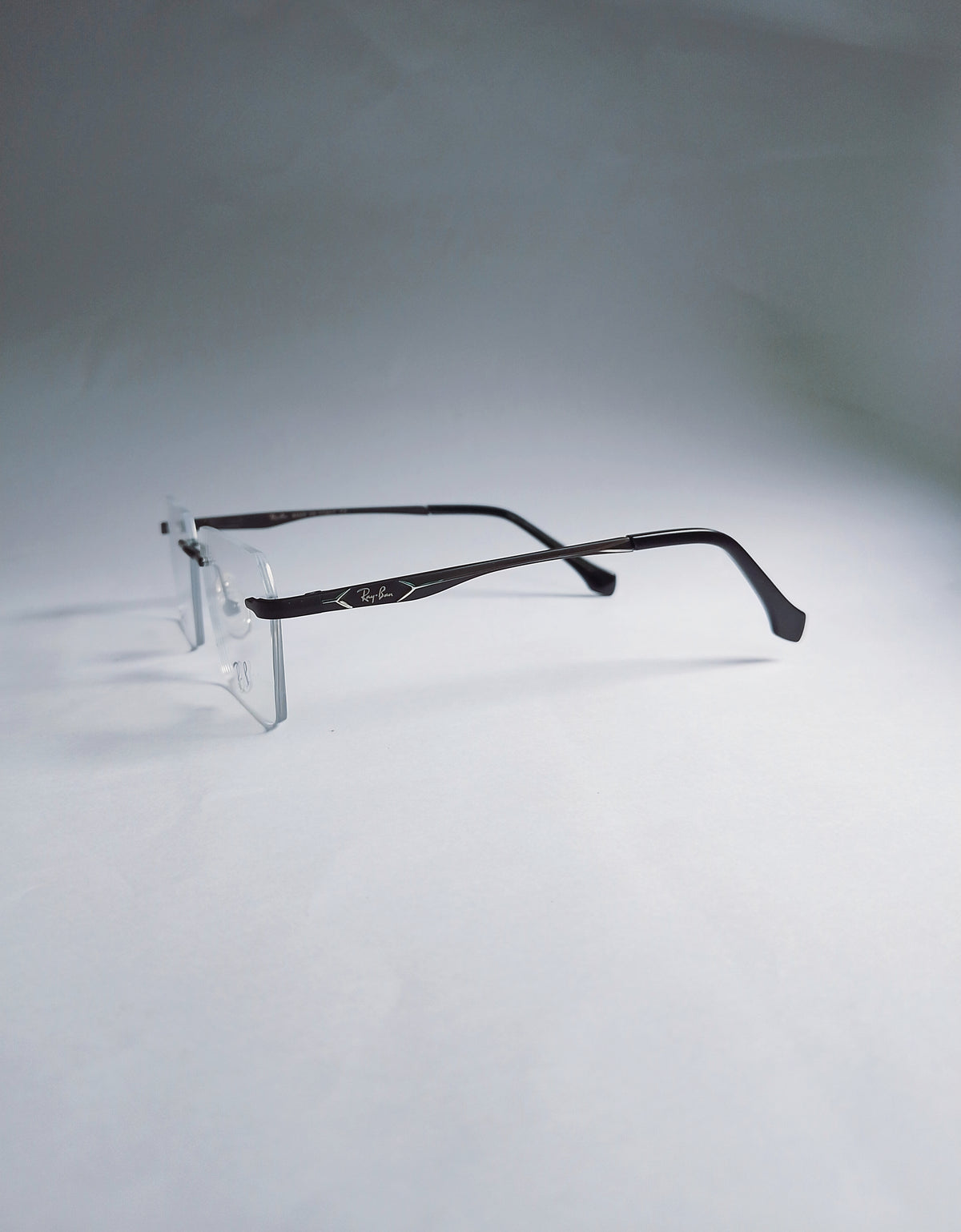 A pair of rimless eyeglasses with dark brown arms and clear lenses, displayed on a clear stand against a light gray background.